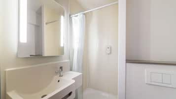 Un baño con un lavamanos blanco, un espejo, una cortina de ducha e interruptor de luz en la pared.