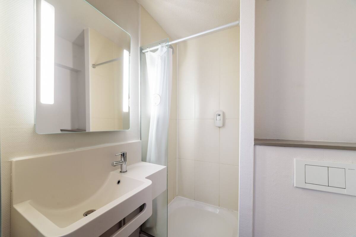A bathroom with a white sink, mirror, shower curtain, and a light switch on the wall.
