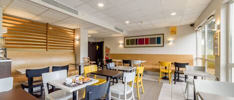 A modern dining area with multiple tables and chairs, a wooden slatted wall, and a large window providing natural light.