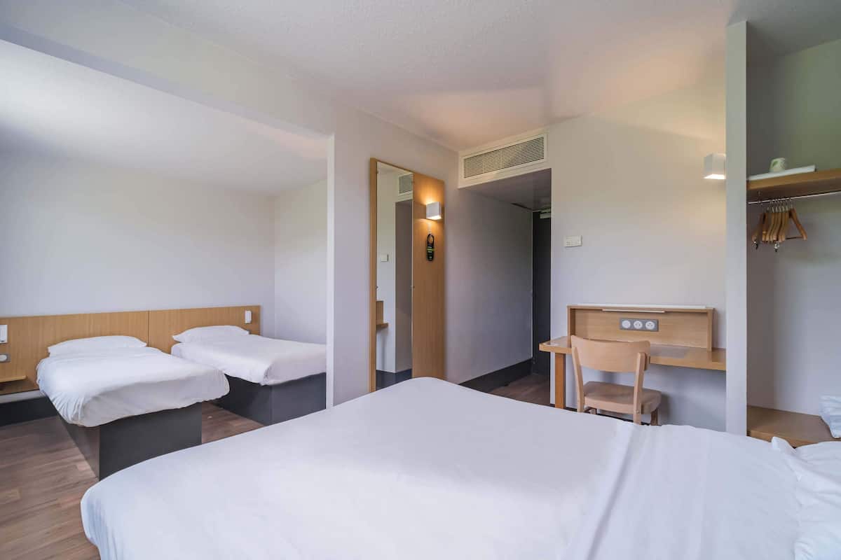 A hotel room with two single beds, a desk with a chair, a wardrobe, and a mirror.