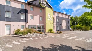 A B&B hotel with a pink and gray facade, a green entrance, and a parking lot. - B&B HOTEL Belfort (Belfort)