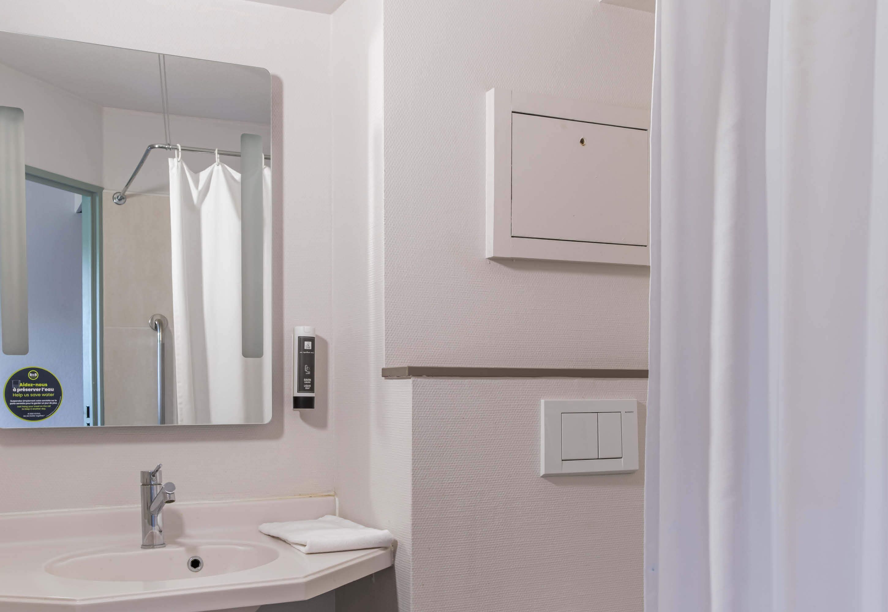 A bathroom with a sink, mirror, shower curtain, and a wall-mounted light switch.