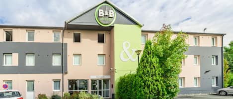Um hotel tipo bed and breakfast com fachada verde e bege, uma placa de boas-vindas e um carro estacionado em frente.
