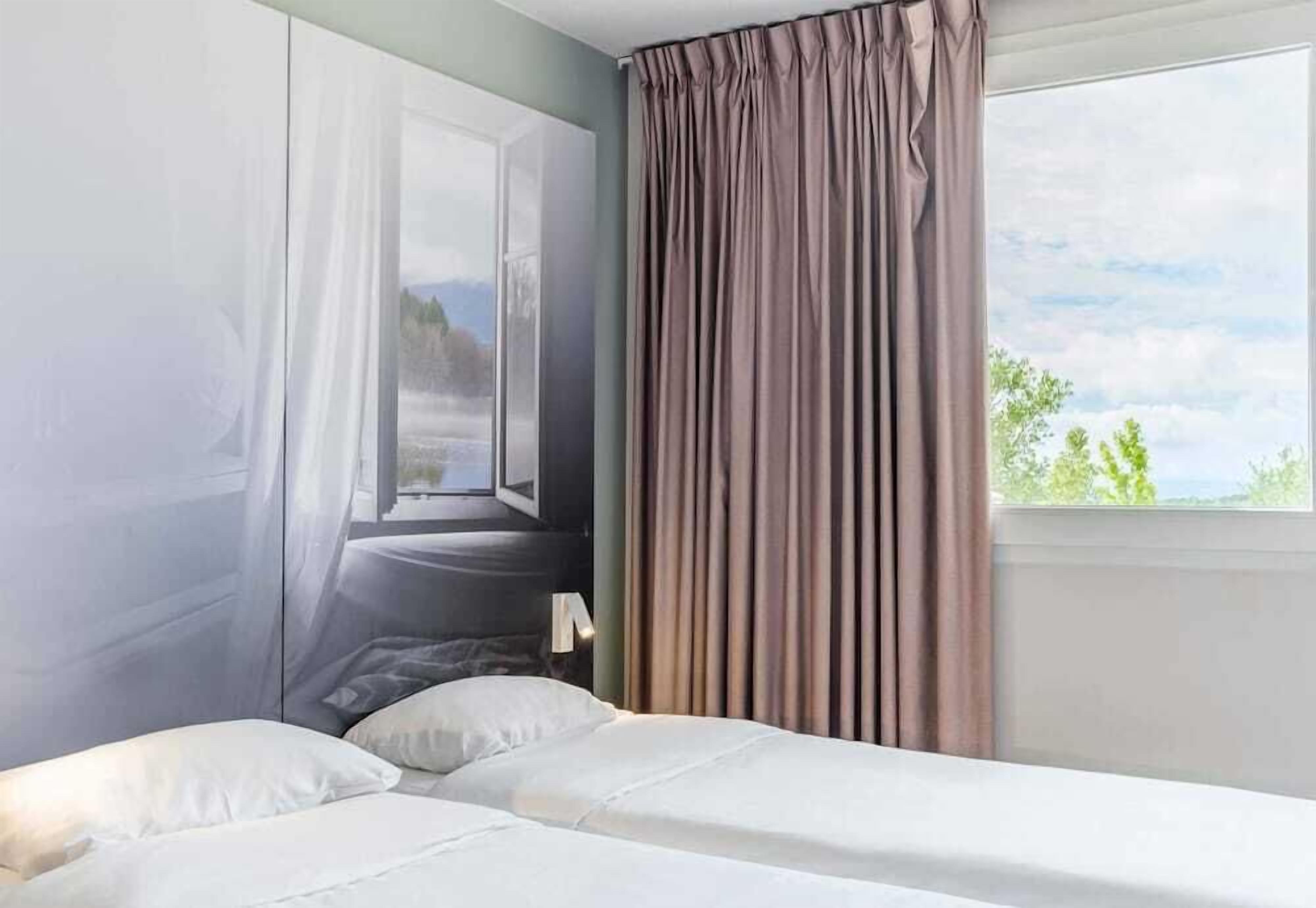A hotel room with a bed, a window with curtains, and a view of the outdoors.