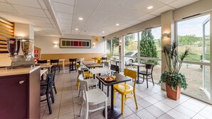 A modern cafe with a variety of seating options, including tables and chairs, and large windows offering a view of the outdoors. - B&B HOTEL Belfort (Belfort)