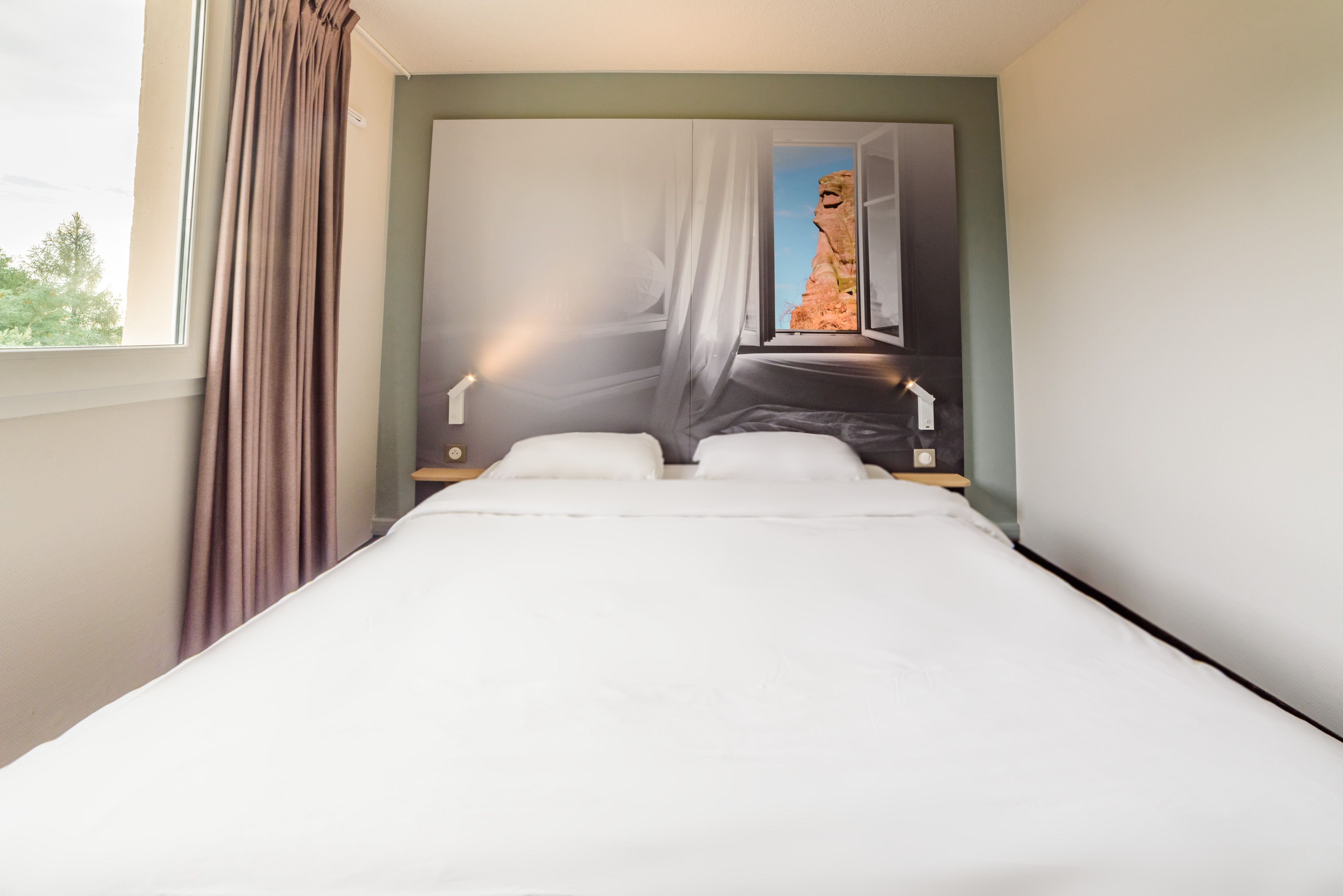Een hotelkamer met een bed, gordijnen, een nachtkastje en een muurschildering.