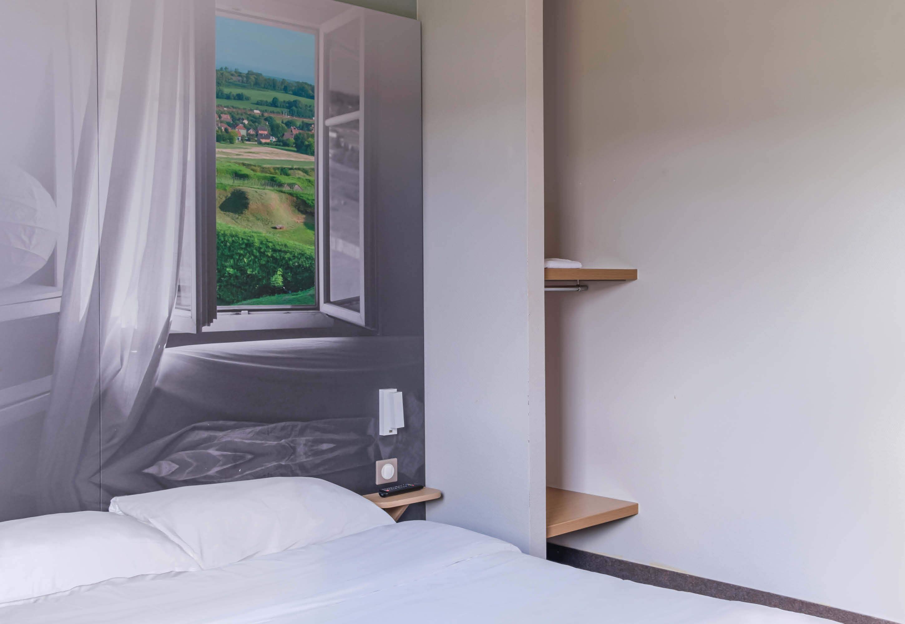 Une chambre à coucher comprenant un lit, une table de chevet, une commode et une fenêtre donnant sur un paysage verdoyant.
