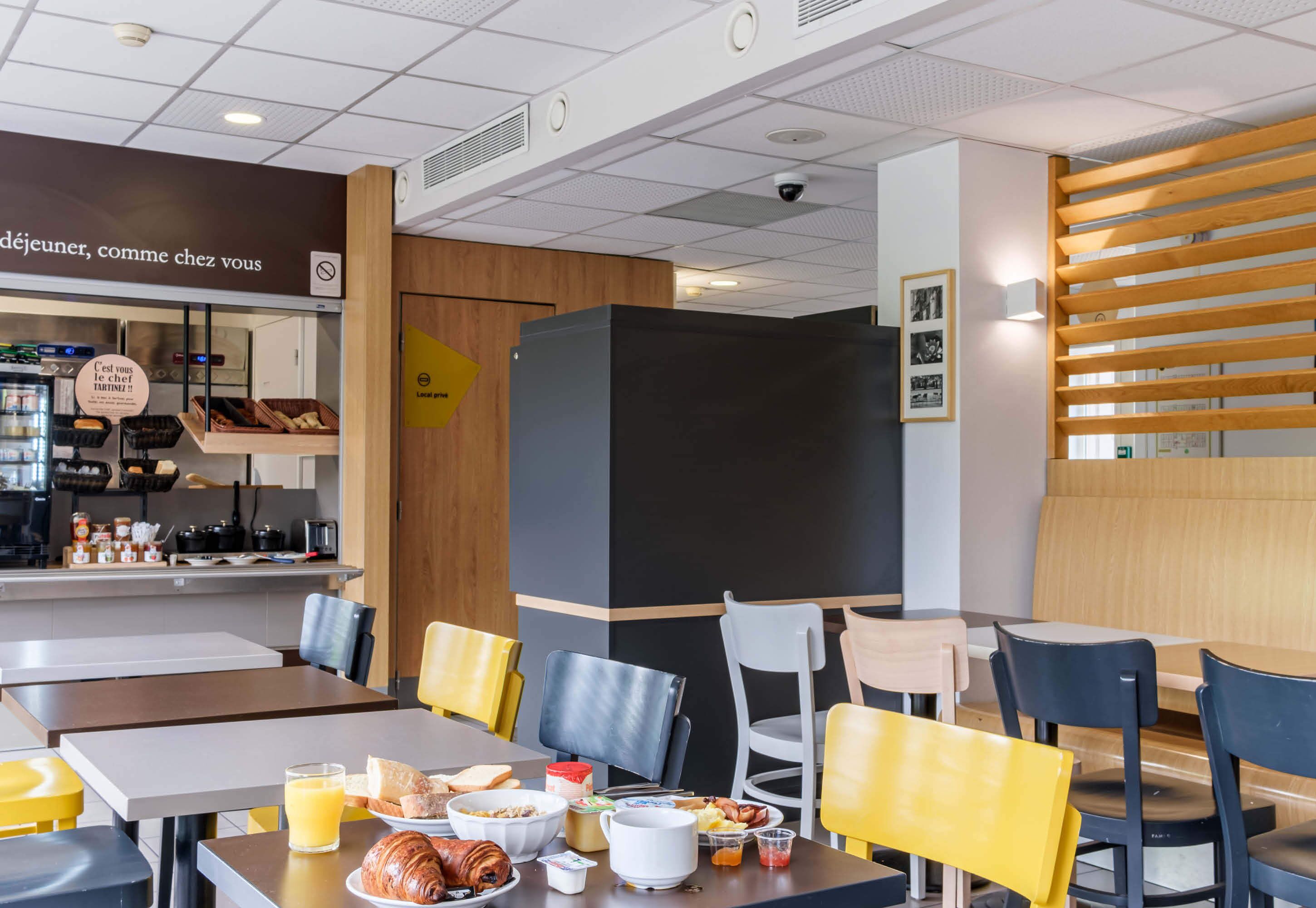 Un espace repas moderne avec des tables et des chaises, un coin cuisine équipé et un comptoir où sont présentés des produits alimentaires.