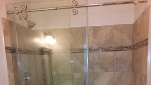 Een douchecabine met glazen wanden, een wit toilet en een douchekop.