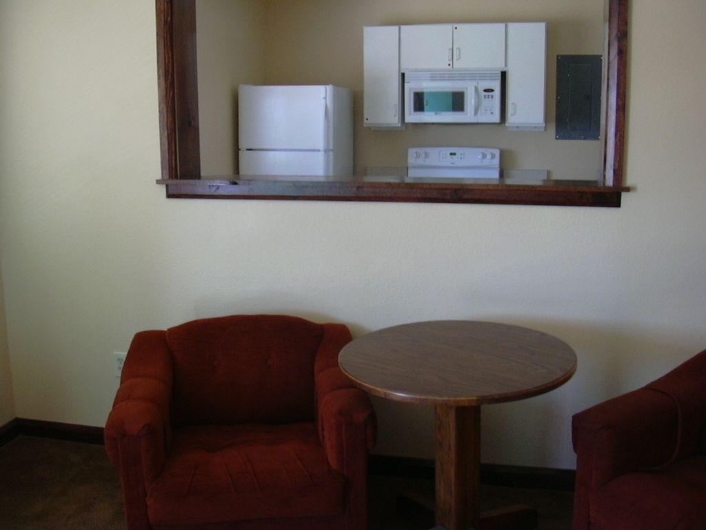 A compact room with a kitchenette, two red armchairs, and a small wooden table.