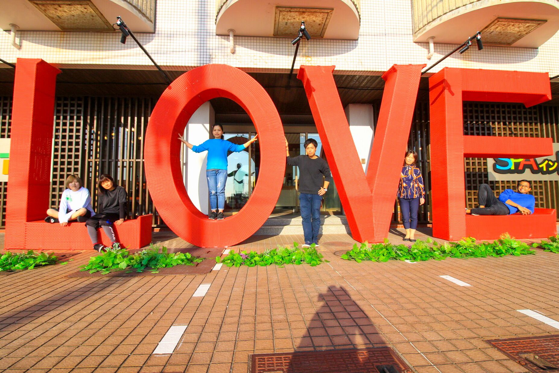 A building entrance with large red letters spelling "LOVE" and people sitting and standing in front.