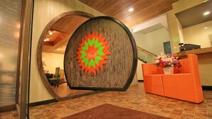 A reception area with a wooden wall, a large mirror, an orange sofa, and a flower arrangement. - Spa Inn Shirahama (Shirahama)