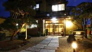 A traditional Japanese-style building with a stone pathway leading to the entrance, surrounded by well-maintained trees and a small garden area. - Jinpuso (Miyazu)