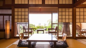 A traditional Japanese room with tatami flooring, a low table, and sliding doors leading to an outdoor garden. - Jinpuso (Miyazu)