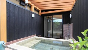 A modern outdoor hot tub area with a wooden pergola overhead, a glass door leading to a covered patio, and a tiled floor surrounding the hot tub. - Jinpuso (Miyazu)