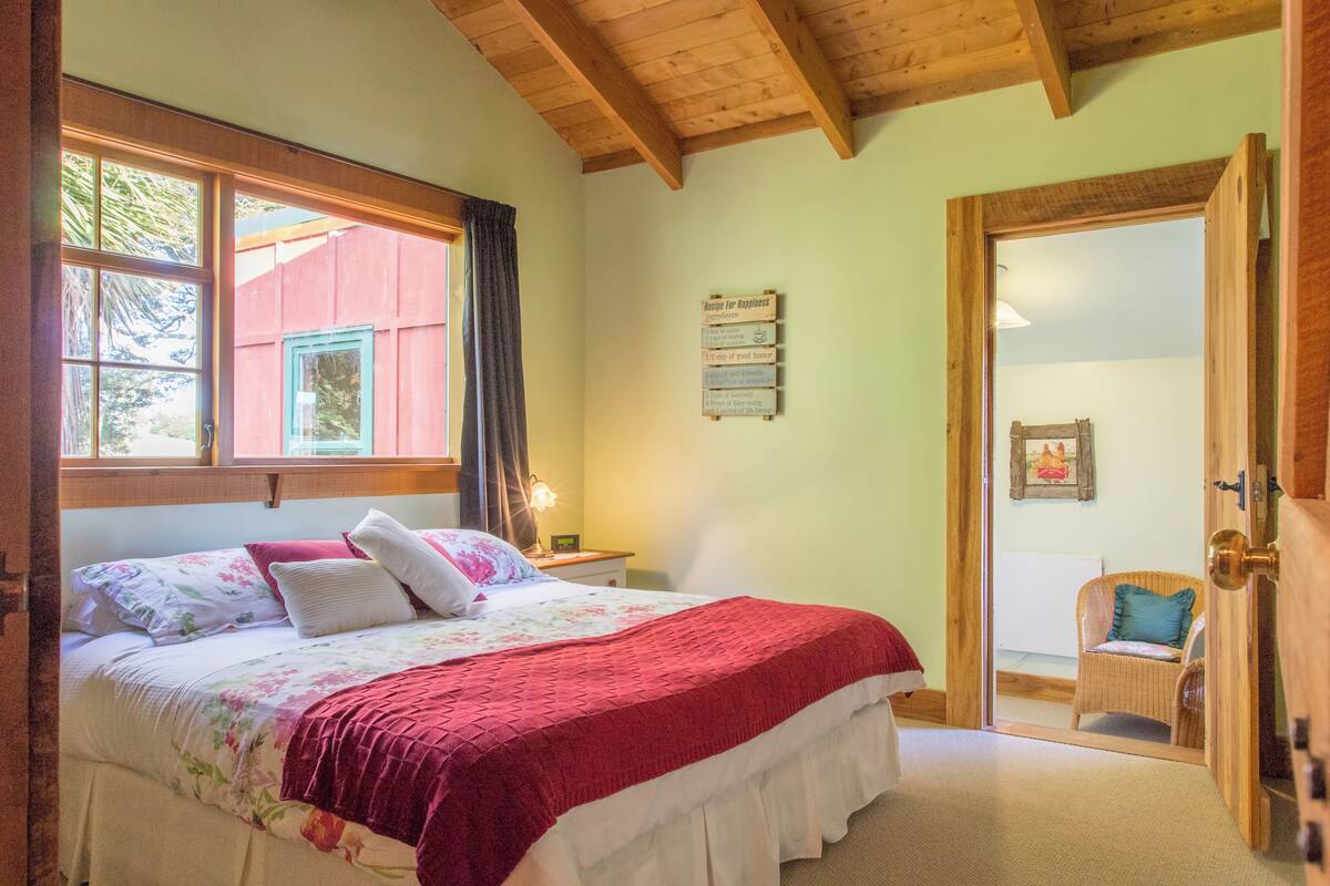 Un dormitorio con una cama grande, una mesita de noche, una ventana con cortinas, una puerta que da a otra habitación y un cartel en la pared.
