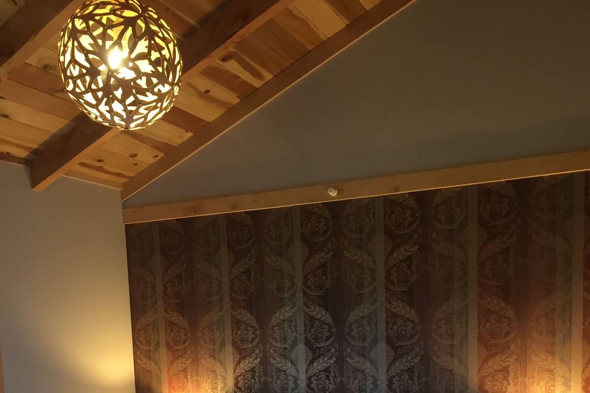 Un dormitorio con una cama grande, dos lámparas de noche, un papel tapiz estampado y techo de madera.