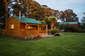 A wooden cabin with a green roof, surrounded by a well-maintained lawn and various trees. - The River Lodge (Ohakune)