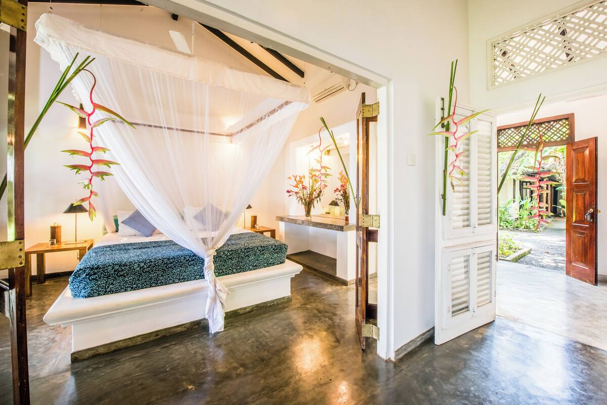 A bedroom with a canopy bed, bedside tables, and a view of the garden.