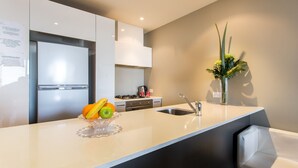 A modern kitchen with a white countertop, a sink, and a stove. There is a fruit bowl with bananas and oranges on the counter. - ABC Accommodation - Spencer Street (Melbourne)