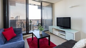 A modern living room with a sofa, a coffee table, a TV, and a balcony with large windows. - ABC Accommodation - Spencer Street (Melbourne)