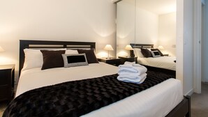 A hotel room with a large bed, two bedside tables with lamps, a mirror, and a door to the right. - ABC Accommodation - Spencer Street (Melbourne)