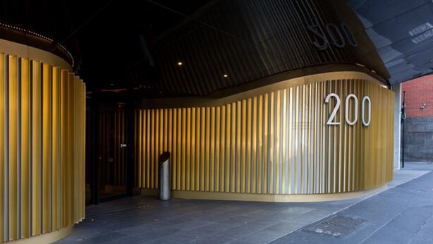A modern building entrance with a curved facade, the number '200' prominently displayed, and a trash bin in front. - ABC Accommodation - Spencer Street (Melbourne)