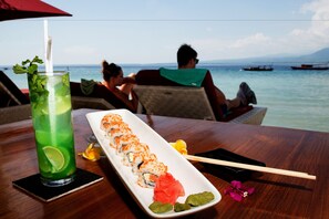 A sushi platter with chopsticks and a drink on a table with a view of the sea. - Bel Air Resort & Spa (Gili Air)