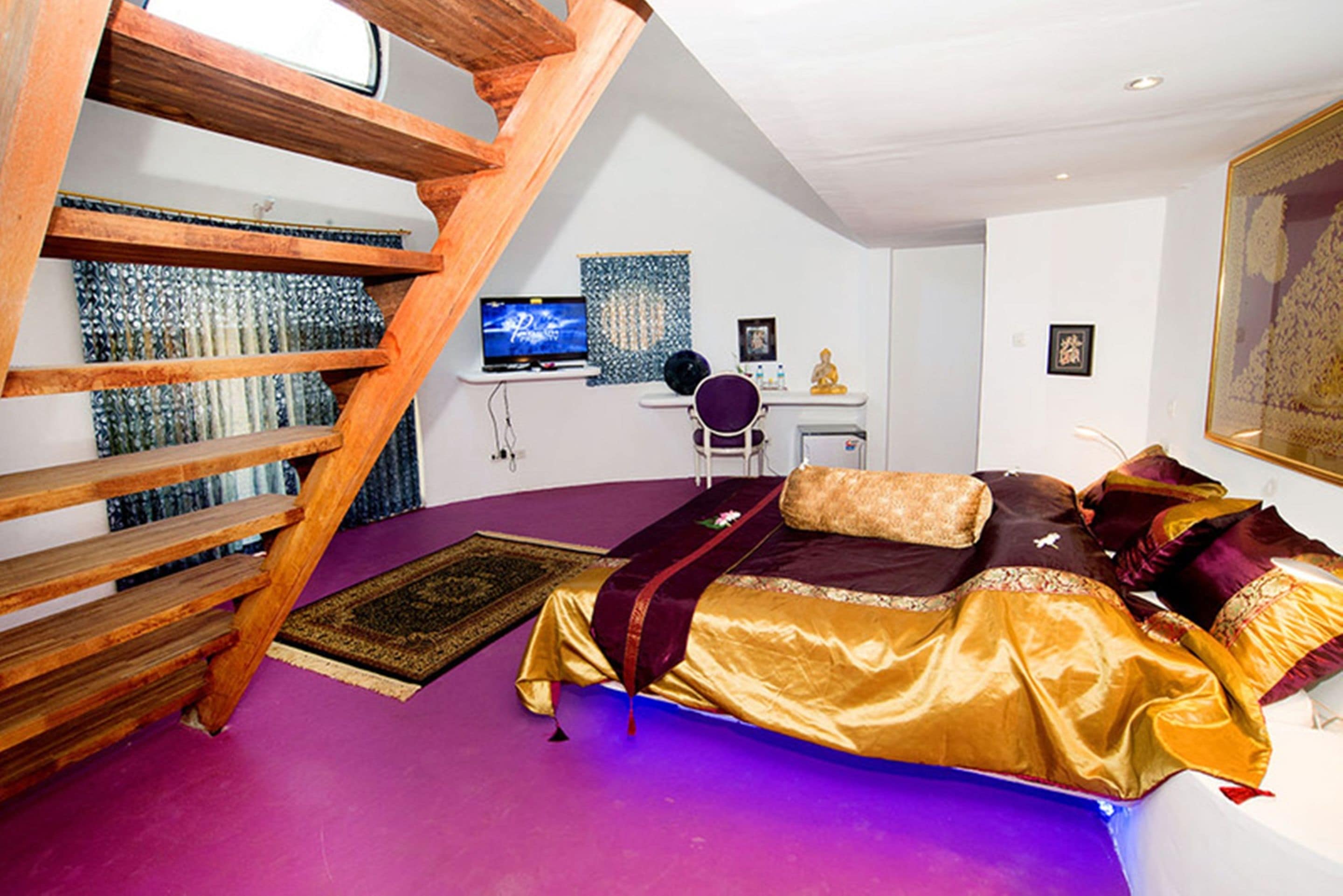 A bedroom with a bed, a desk, a computer, and a staircase.