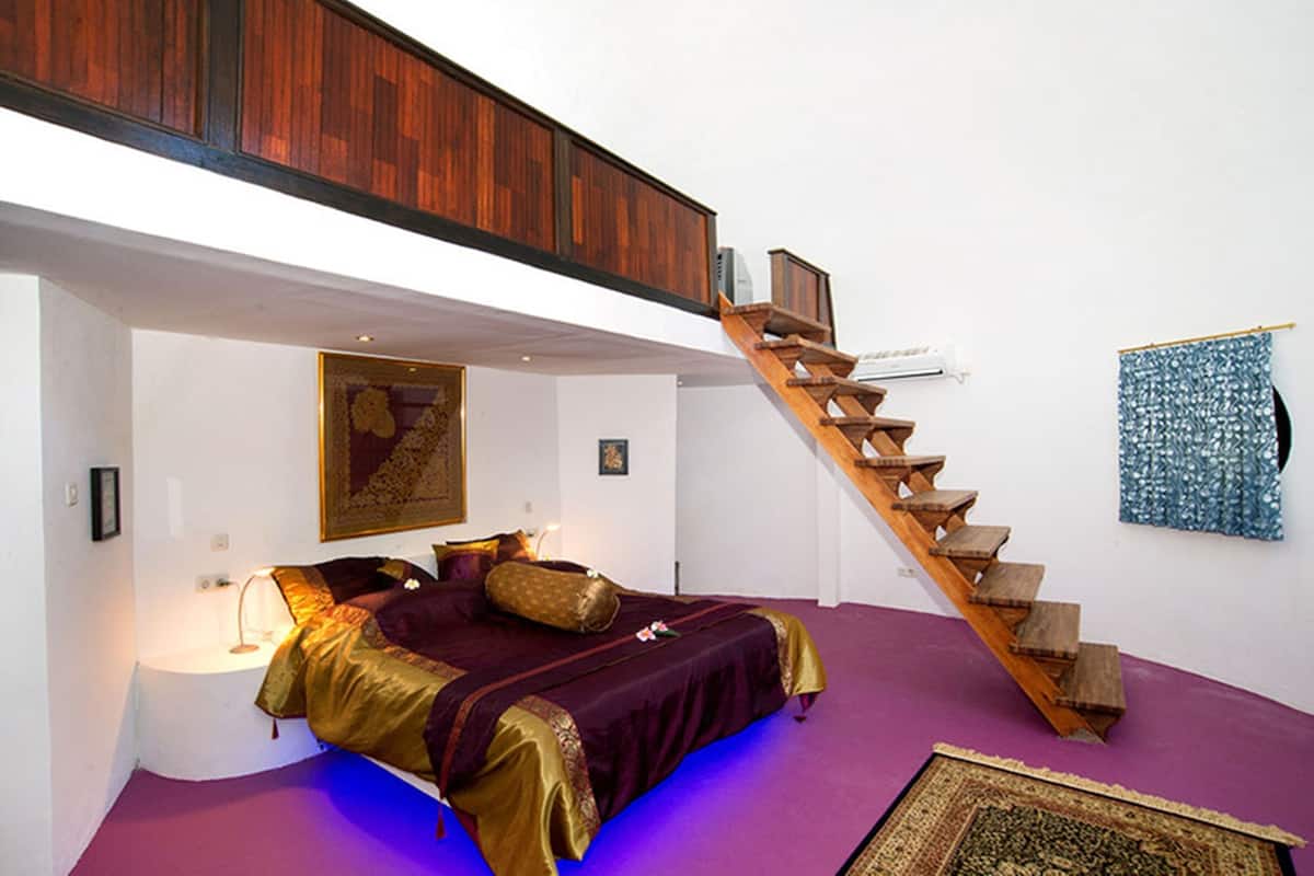 A bedroom with a bed, a staircase, and a wall-mounted air conditioner.