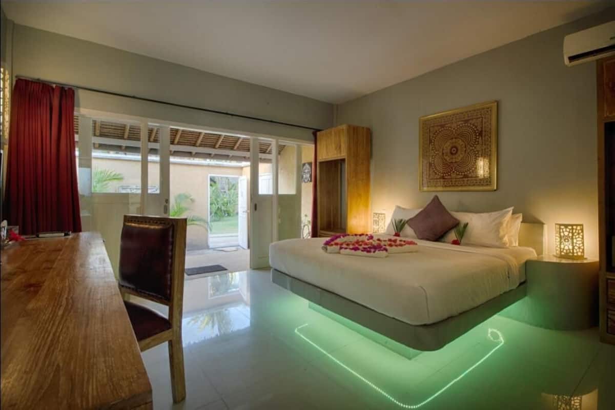 A bedroom with a bed, a wooden table, and a chair. There is a door leading to a balcony.