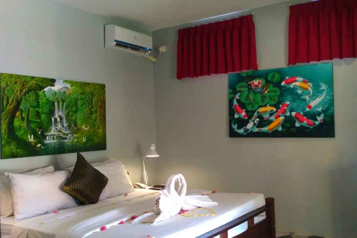A bedroom with a bed, a wall-mounted air conditioner, and two paintings.