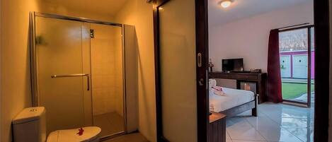 Habitación de hotel con inodoro, ducha y cama con televisor.