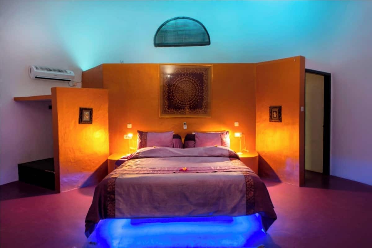 A room with a bed, a wall-mounted air conditioner, and a decorative wall piece.