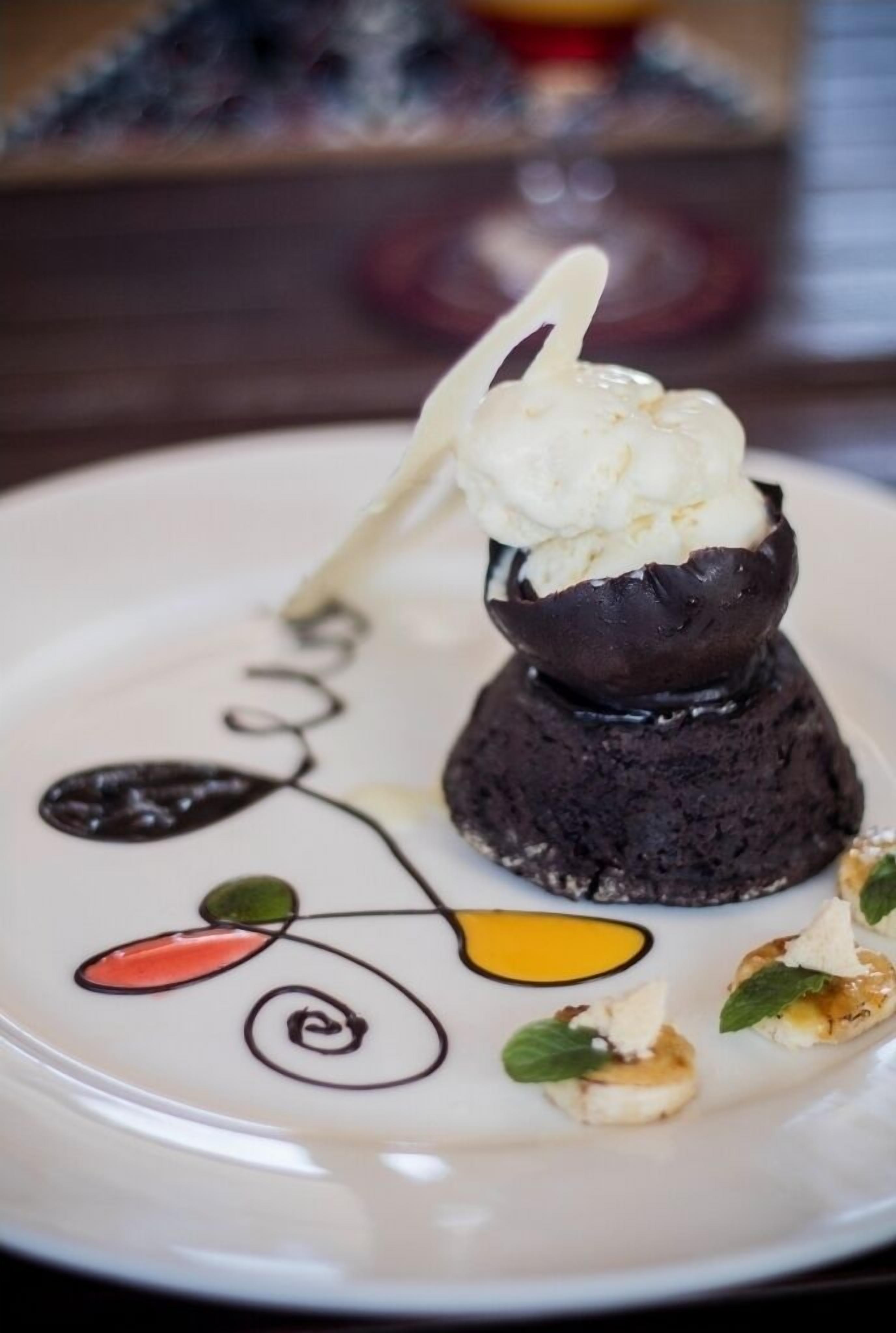 Un plato de postre con pastel de chocolate, una bola de helado y adornos.