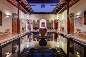 Una piscina interior espaciosa con un jarrón decorativo en el centro, bancos de madera y un techo de baldosas.