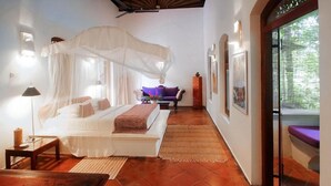 A bedroom with a bed under a canopy, a nightstand, a bench, and a view of the outdoors. - Apa Villa Illuketia (Padinnoruwa)