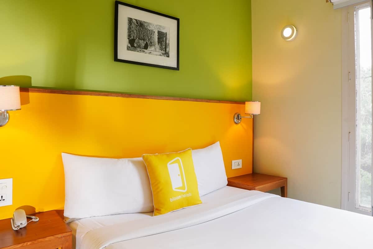 A hotel room with a bed, a bedside table with a phone, a nightstand with a lamp, and a window with a view.