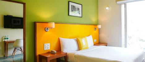A hotel room with a bed, a desk with a chair, a television, and a window with an air conditioning unit.