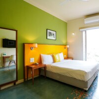 A hotel room with a bed, a desk with a chair, a television, and a window with an air conditioning unit.