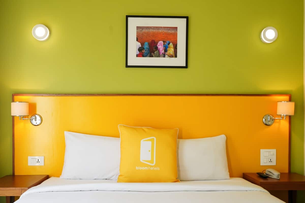 A hotel room with a yellow headboard, white bedding, and a framed picture on the wall.