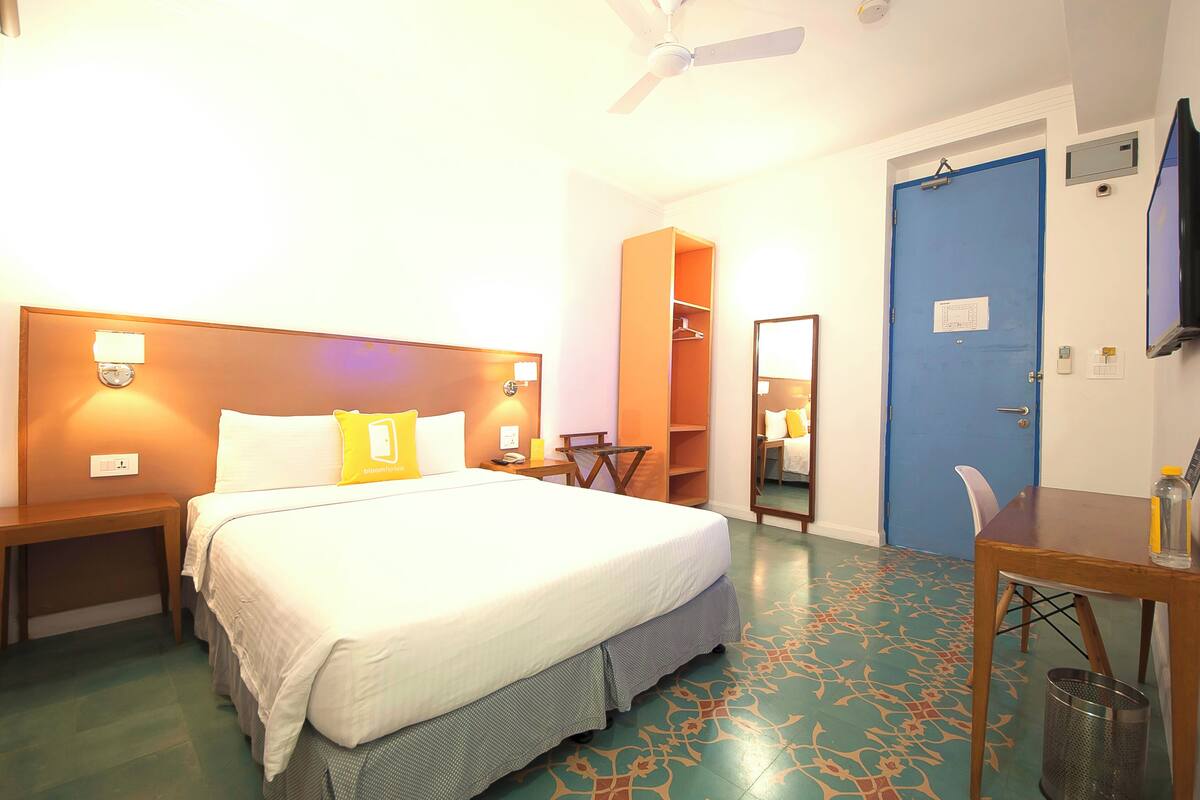 A hotel room with a bed, bedside tables, a desk, a chair, a wardrobe, and a ceiling fan.