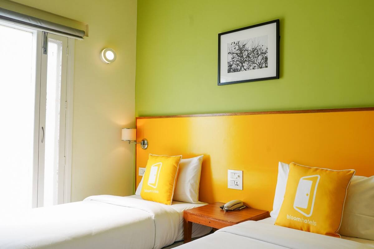 A hotel room with two beds, a bedside table with a phone, and a wall-mounted light.
