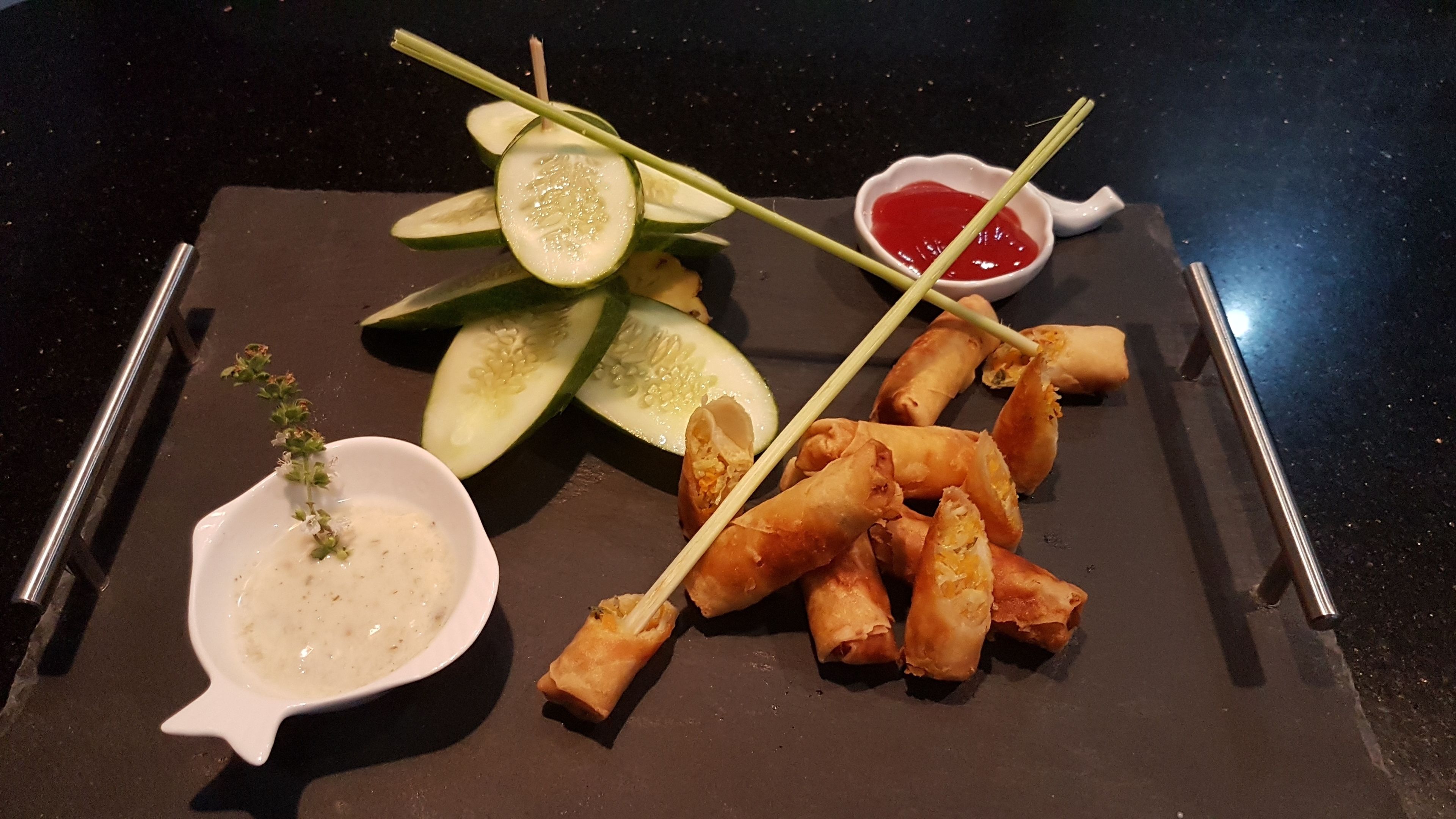 Une assiette avec des rouleaux de printemps, des tranches de concombre et un petit bol de sauce.