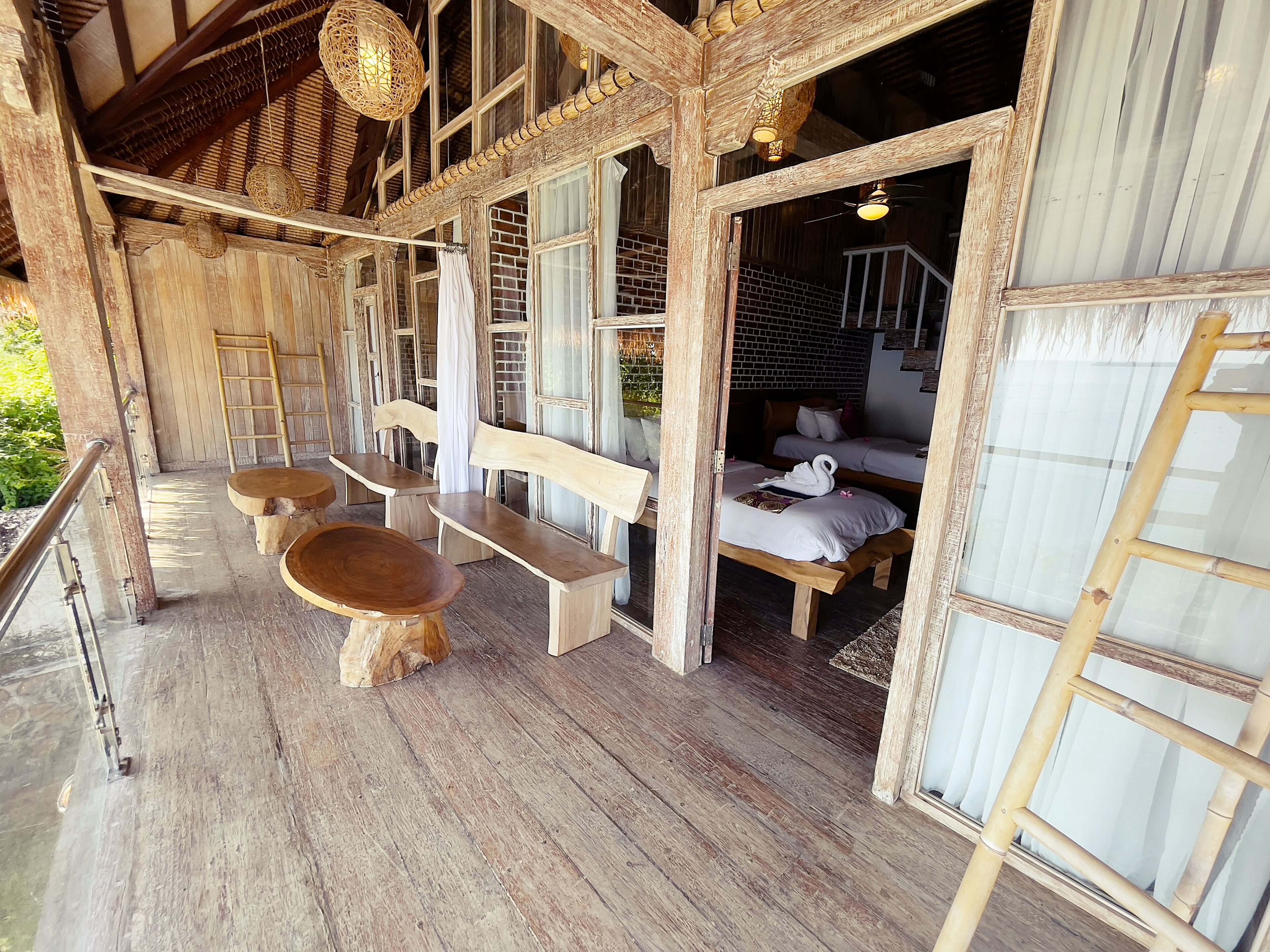 A rustic wooden cabin with a wooden bench seating area, a bed with white bedding, and a ladder.