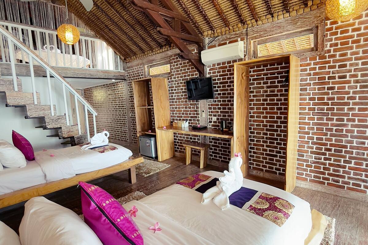 Un dormitorio con cama, almohadas, escritorio, silla, televisor y una escalera.