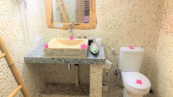 A bathroom with a pebble-textured wall, a granite sink, a wooden-framed mirror, a toilet, and a bamboo ladder.