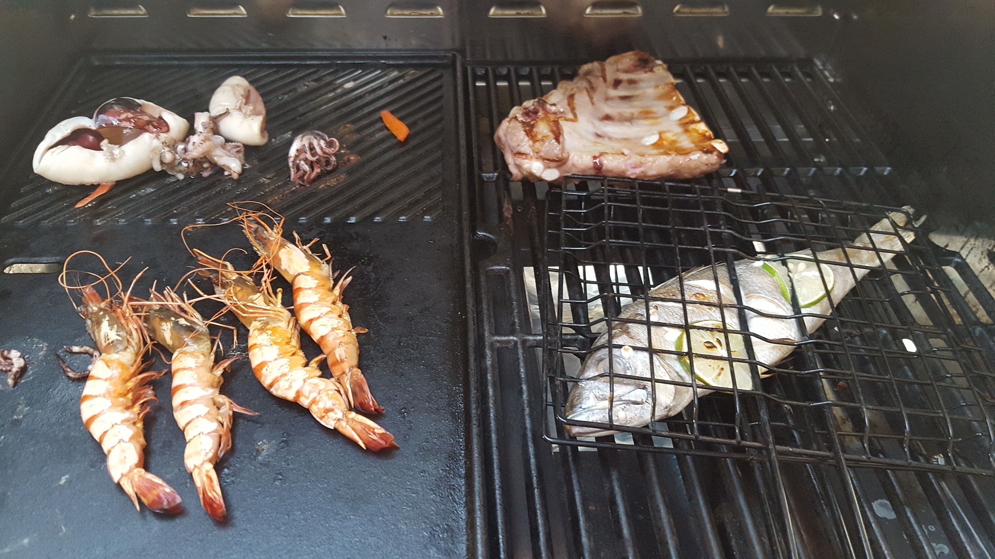 A grill with seafood including shrimp, fish, and a piece of meat.