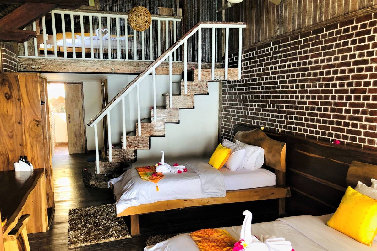 Una habitación de hotel rústica con una escalera de madera, una pared de ladrillo y dos camas con sábanas blancas y almohadas amarillas.