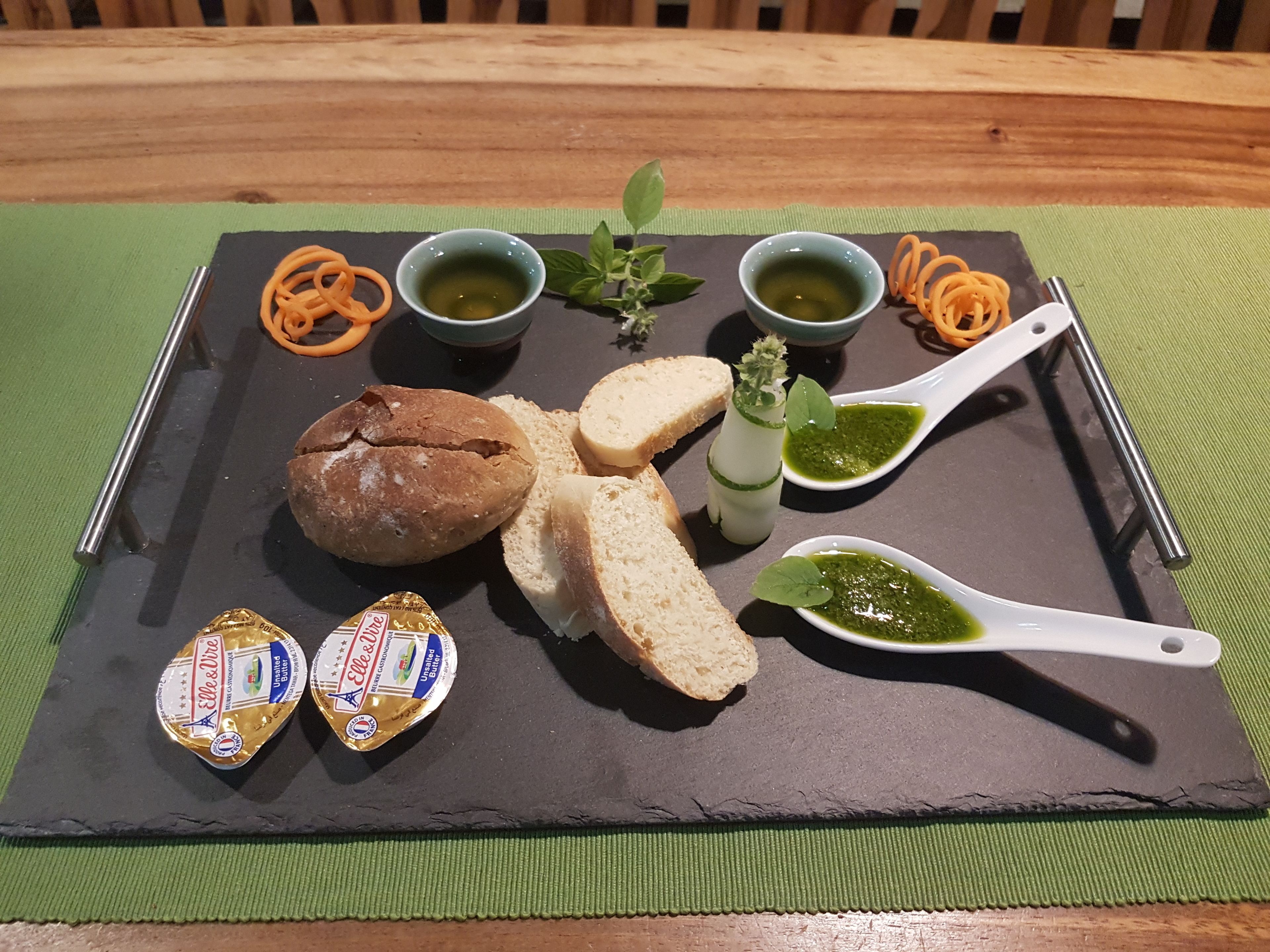 Eine Platte mit Wurstwaren, Brot, Käse und grünen Soßen auf einer Schiefertafel.